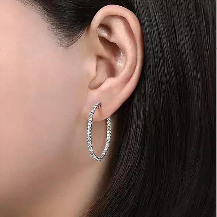 Sparkling diamond hoop earrings, one-inch size, worn against dark hair.