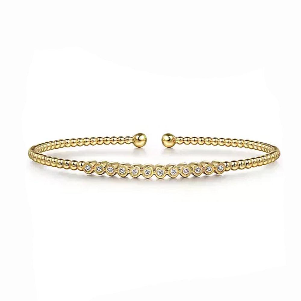 Beaded gold bangle bracelet featuring a row of bezel-set diamonds.