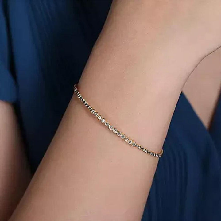 14K gold bangle bracelet featuring a row of bezel-set diamonds.