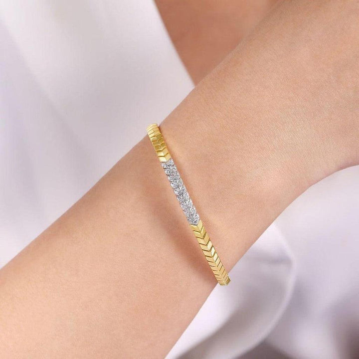 Gold chevron cuff bracelet adorned with diamonds, shown on a wrist.