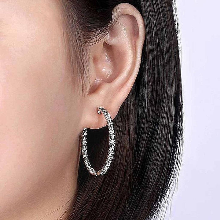 Sparkling diamond hoop earrings worn against dark hair.