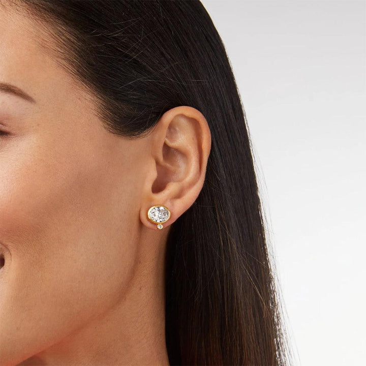 Gold stud earrings featuring an oval-cut clear gemstone and a smaller accent stone.
