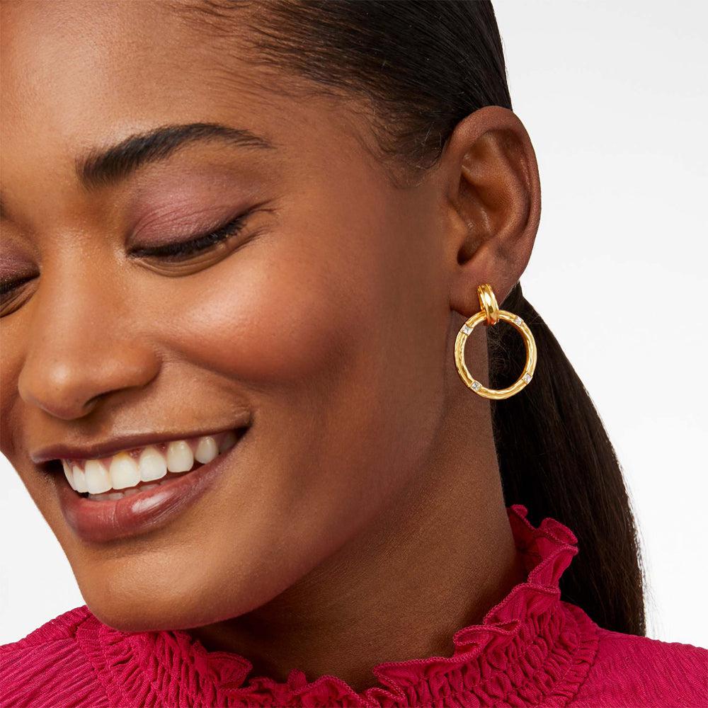 Gold circular earrings with clear stones, worn by a woman.