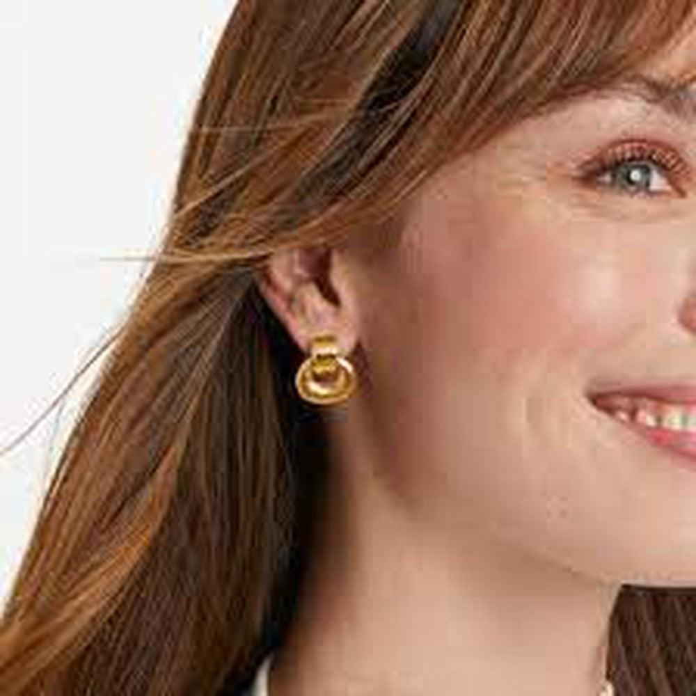 Gold doorknocker-style earrings on a woman's ear, close-up view.