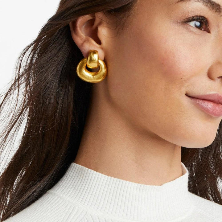 Gold doorknocker earrings worn by a woman; textured, statement piece.