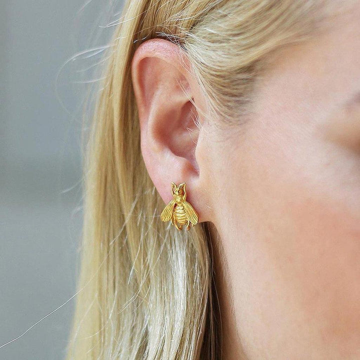 Gold bee stud earrings in a woman's ear.