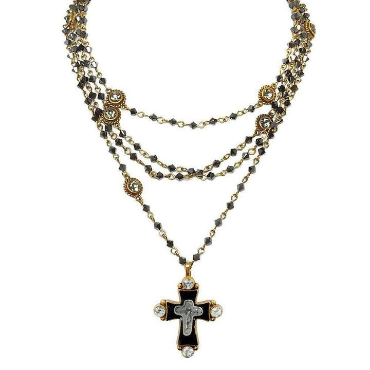 Layered gold necklace with dark gray beads and a black cross pendant adorned with clear crystals.