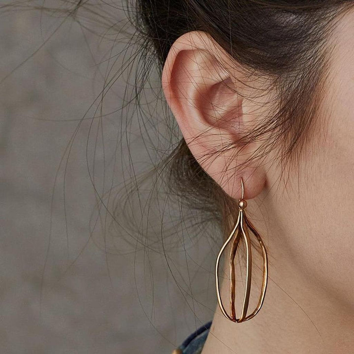 Gold birdcage-style drop earrings on a model's ear.