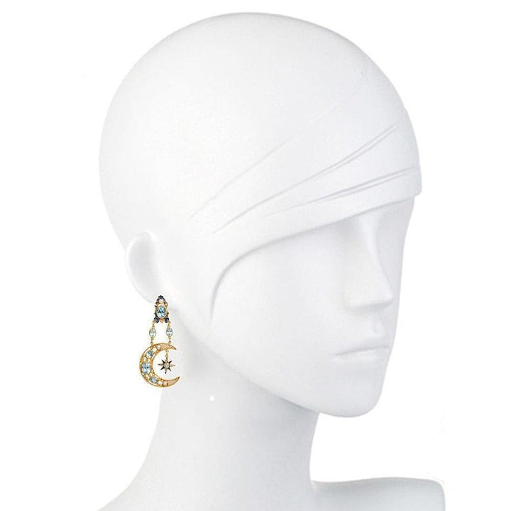 Gold crescent moon earrings adorned with blue topaz, pearls, and a starburst detail on a mannequin.