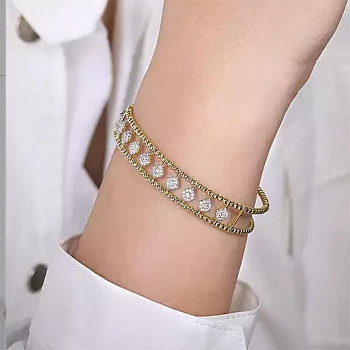 Gold cuff bracelet adorned with sparkling diamond accents, shown on a wrist.