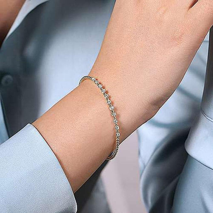 Delicate gold bracelet adorned with small, sparkling diamonds on a woman's wrist.