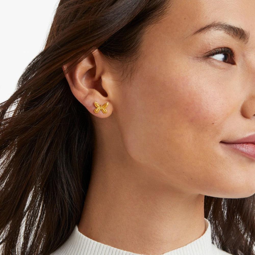 Gold butterfly stud earrings on a woman's ear.