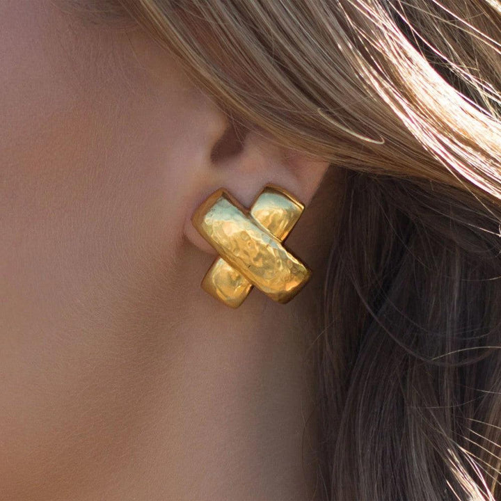 Gold cross-shaped clip-on earrings worn on earlobe.