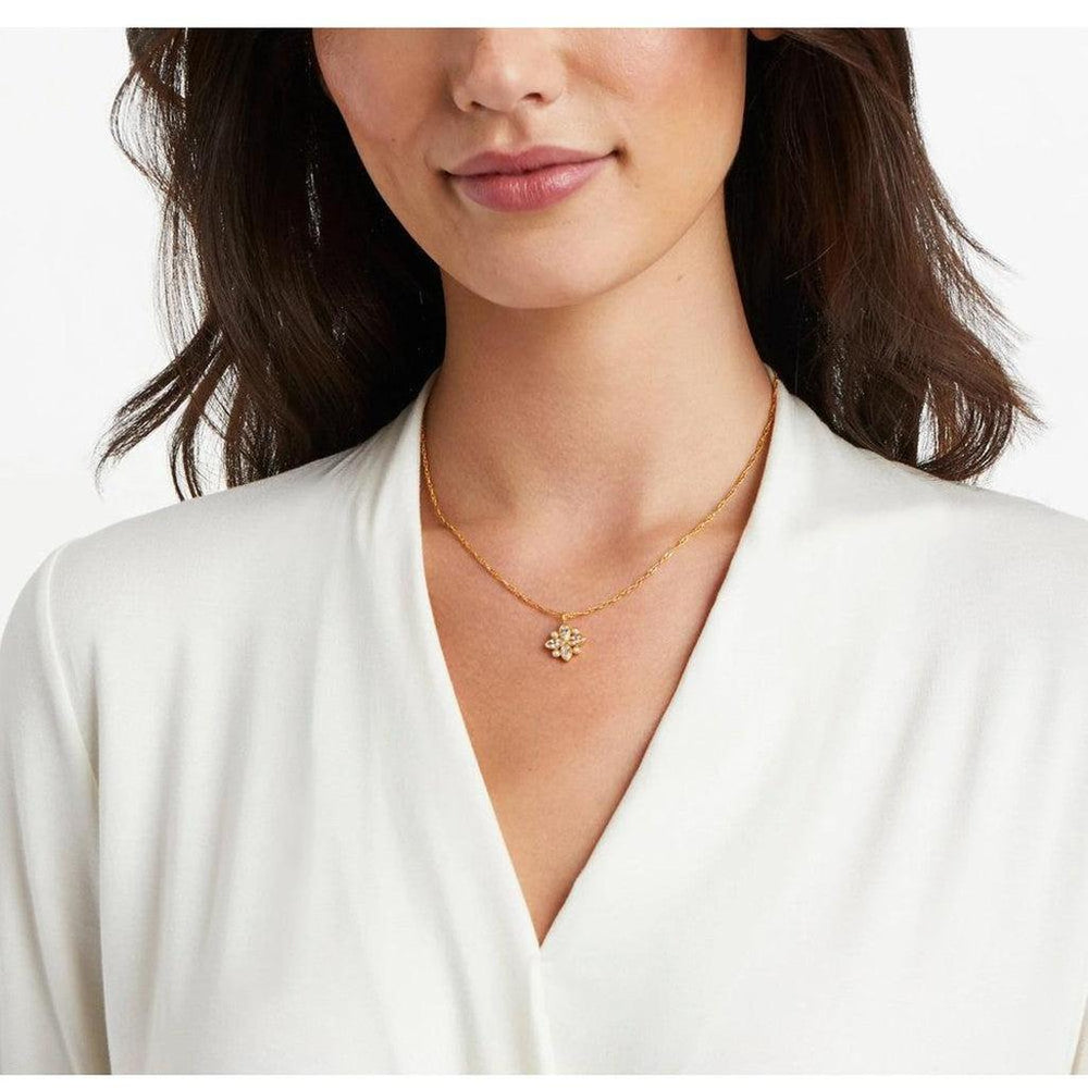 Gold chain necklace with delicate flower pendant; worn by model in off-white top.