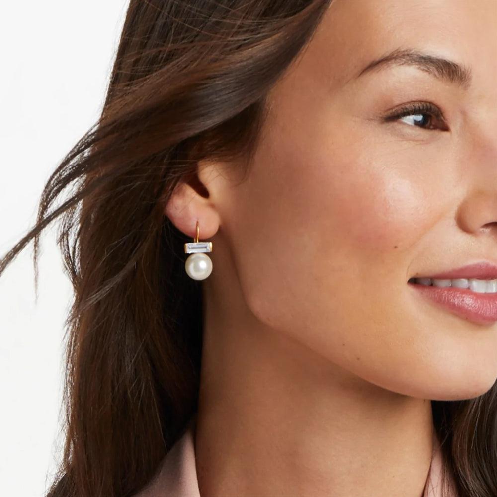 Gold-toned pearl and baguette-cut crystal drop earrings on a model.