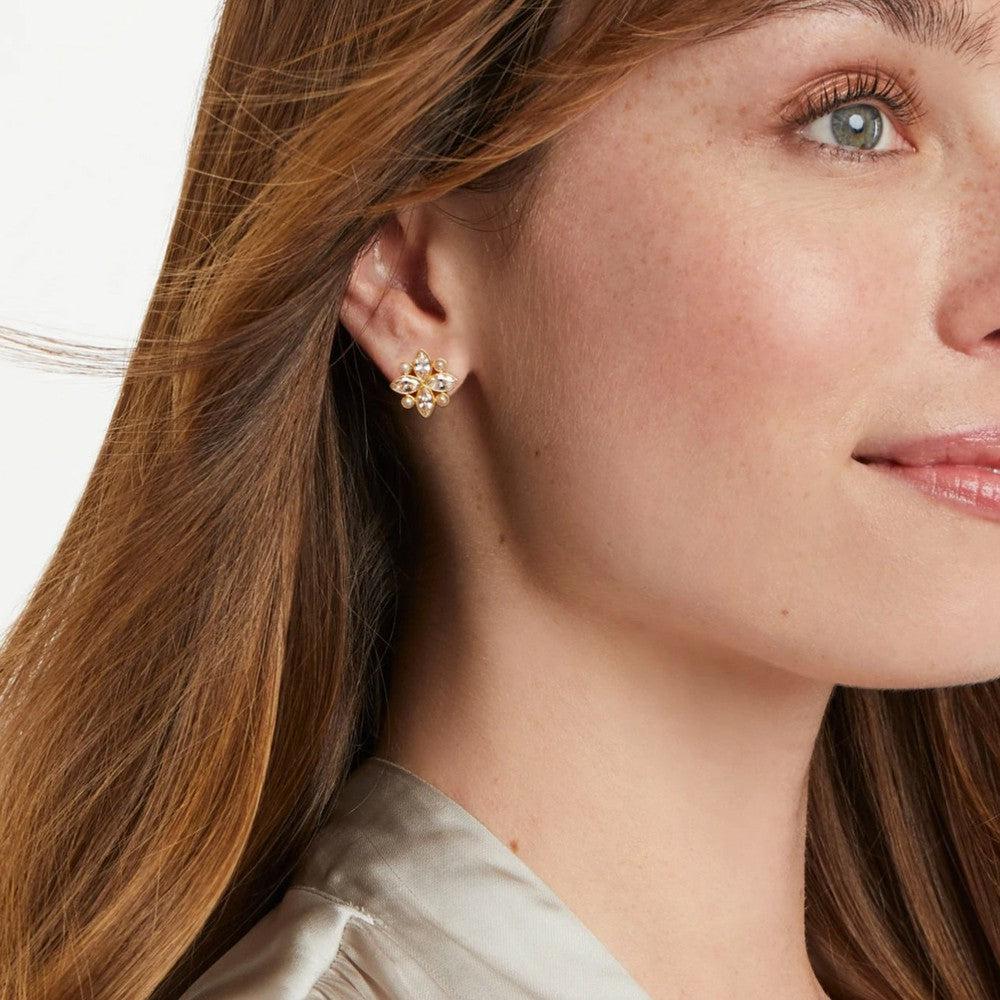 Gold stud earrings with sparkling stones, worn by a woman with long brown hair.