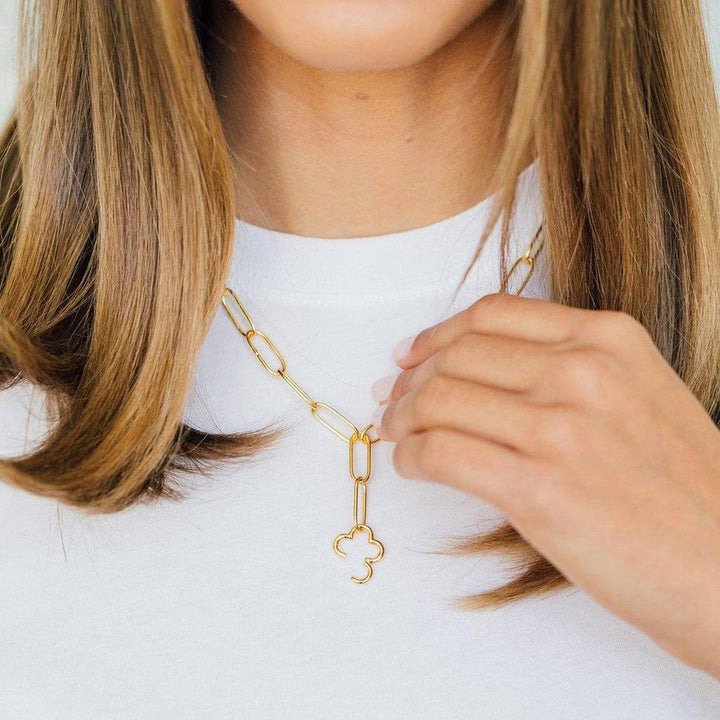 Gold chain necklace with clover charm, worn against a white top.