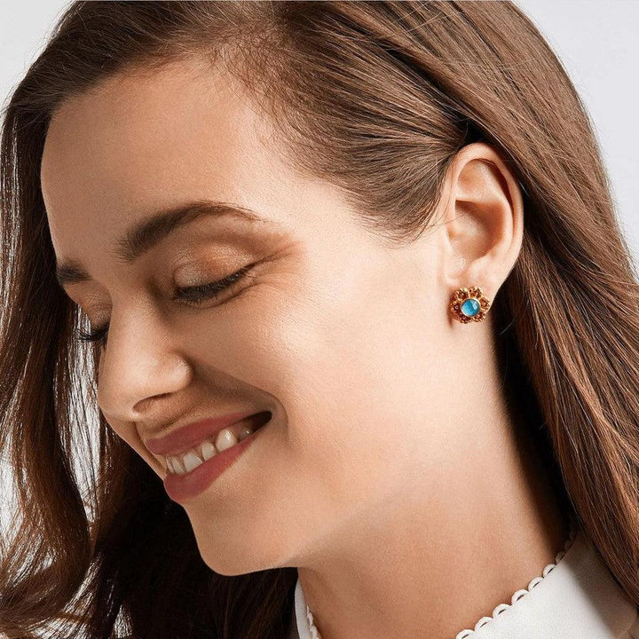 Gold stud earrings with a blue gemstone center, shown on a model's ear.