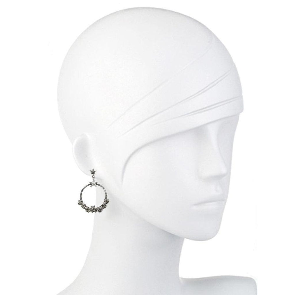 Silver hoop earrings adorned with small dark stones and stars, shown on a mannequin.
