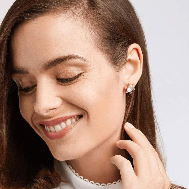 Rose gold stud earrings featuring a textured, pearlescent stone; closeup on model's ear.