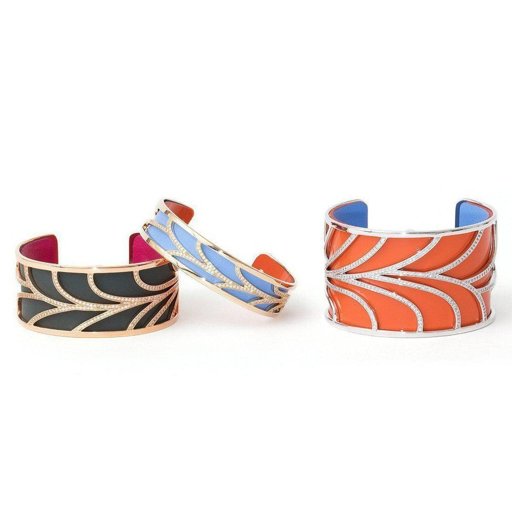 Three wide gold cuffs, one each in black, blue, and orange enamel, adorned with diamond detailing.