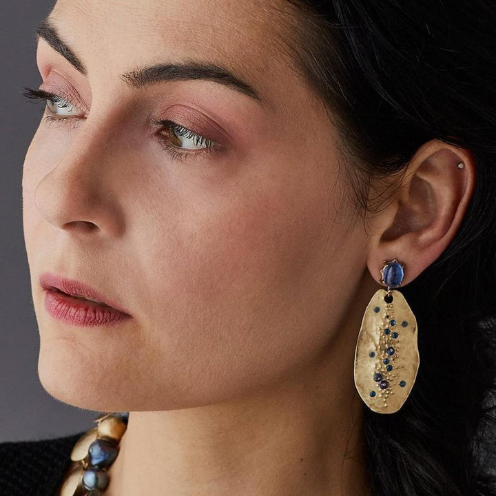 Gold kyanite earrings with blue gemstone accents, worn by a woman.