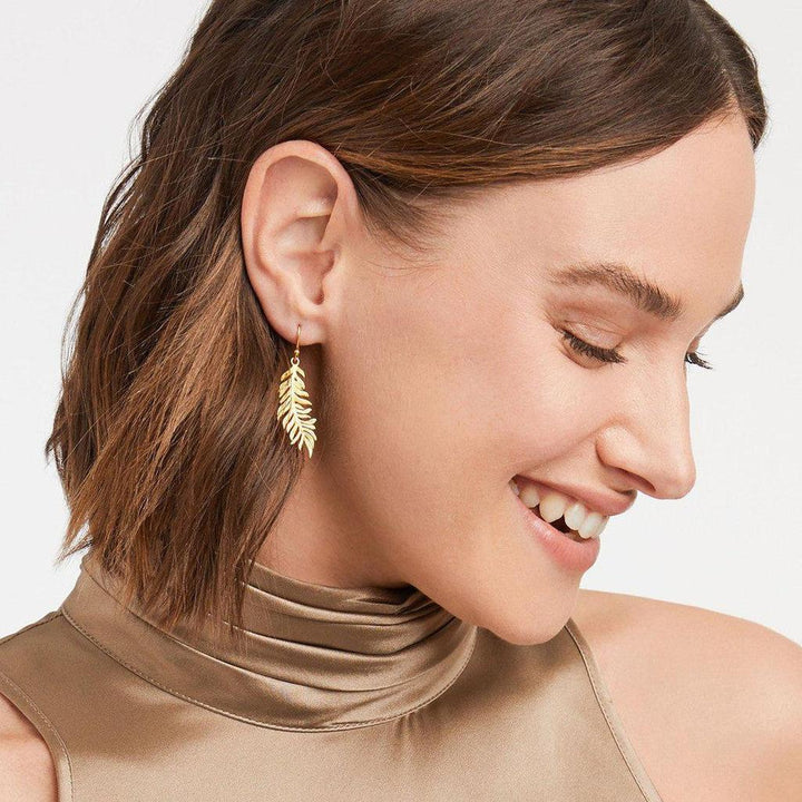 Gold fern leaf drop earrings on model