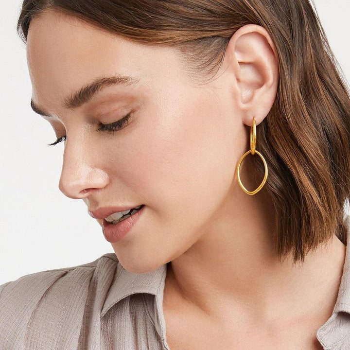 Gold double hoop earrings, textured metal, worn by a woman.