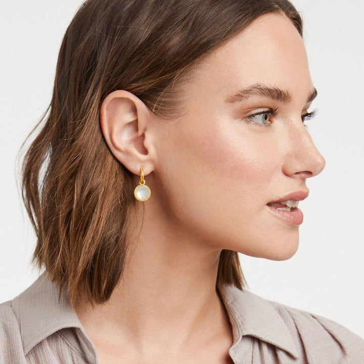 Gold hoop earrings with a white stone charm, worn by a model.