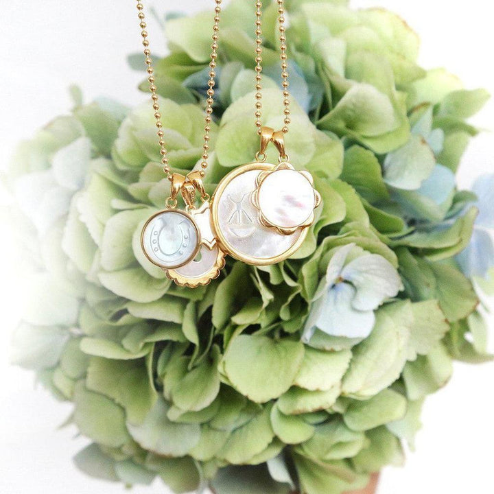 Gold necklaces with mother-of-pearl charms, nestled in a bouquet of hydrangeas.