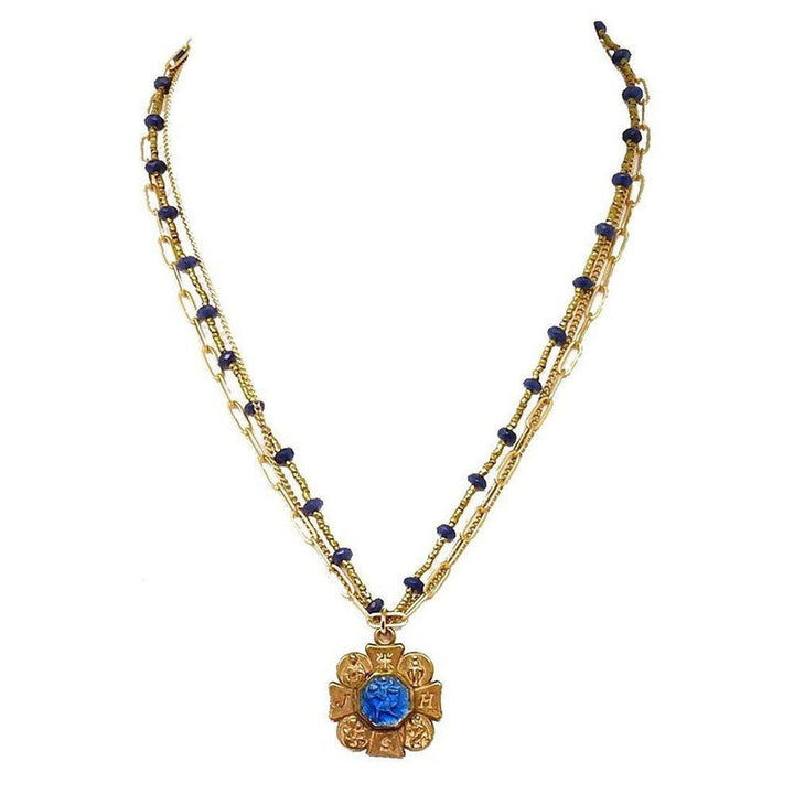 Gold layered necklace featuring a blue gemstone pendant and dark blue beads.