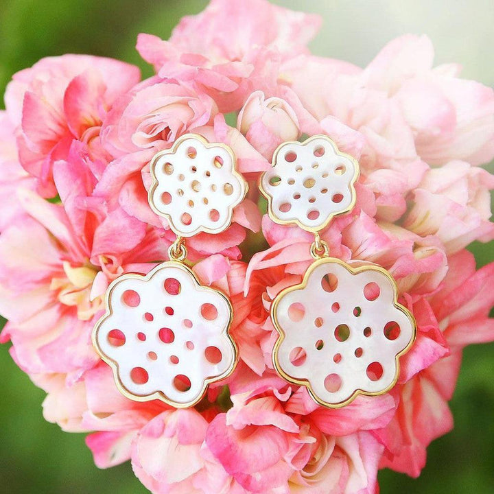 White and gold flower-shaped drop earrings displayed on pink blossoms.