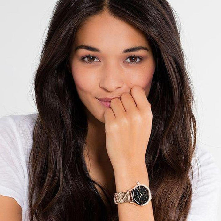 Woman's wrist showcasing rose gold watch with black face and mesh band.
