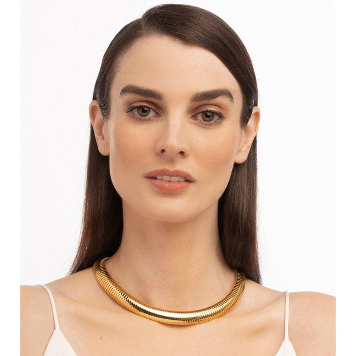 Woman wearing a gold choker necklace against a white background