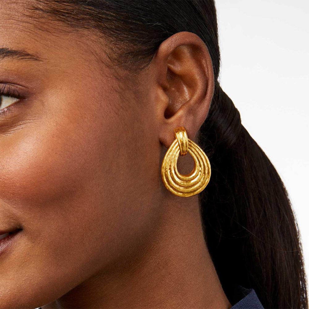 Gold doorknocker-style earrings on a model's earlobe.