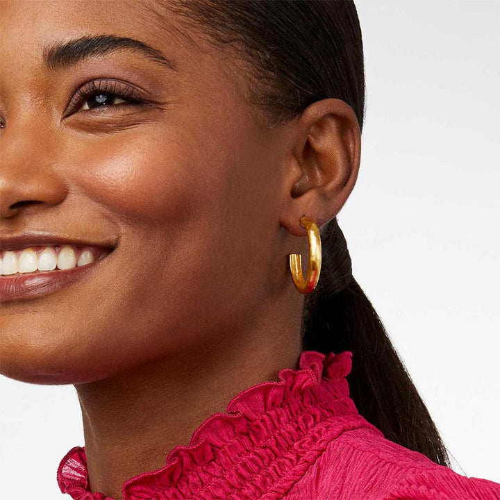 Gold hoop earrings on a model wearing a fuchsia top.