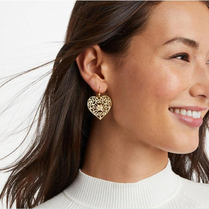 Gold filigree heart earrings with sparkling accents, worn by a woman.