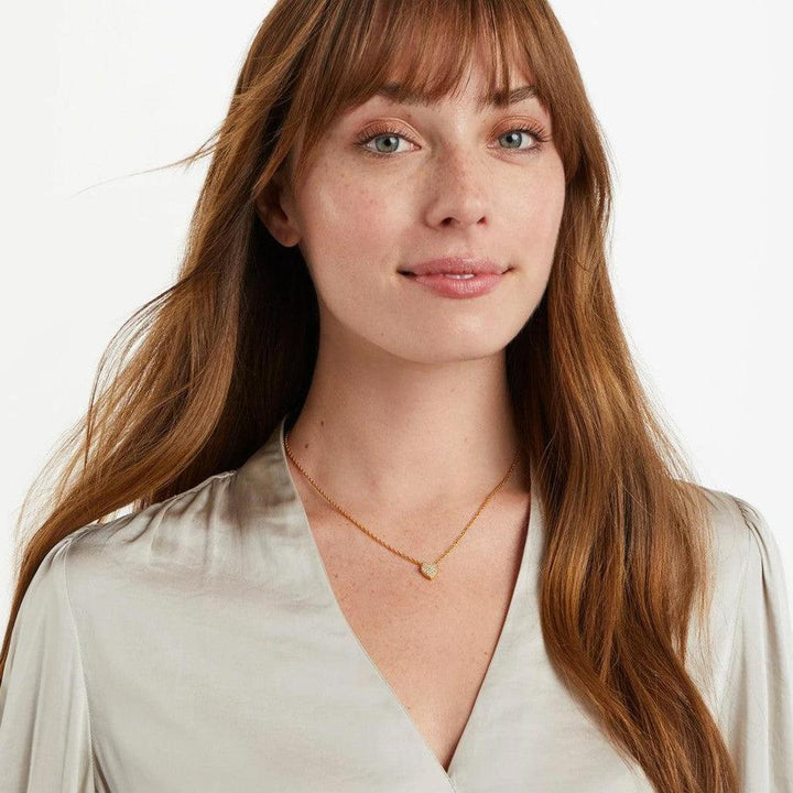 Gold chain necklace featuring a small, pave heart pendant on a woman.