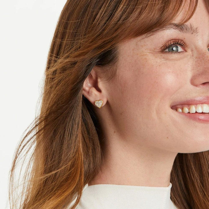Gold heart-shaped stud earrings adorned with sparkling stones, shown on a model.