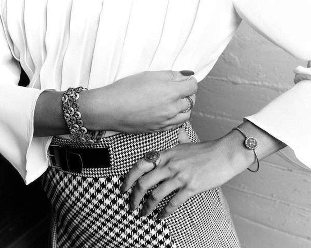 Black and white photo of a woman's wrist wearing a delicate chain bracelet;  the bracelet features a small, detailed circular charm.