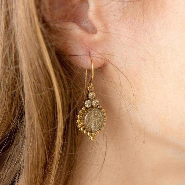 Gold drop earrings featuring a clear stone with antique detailing, worn against blonde hair.