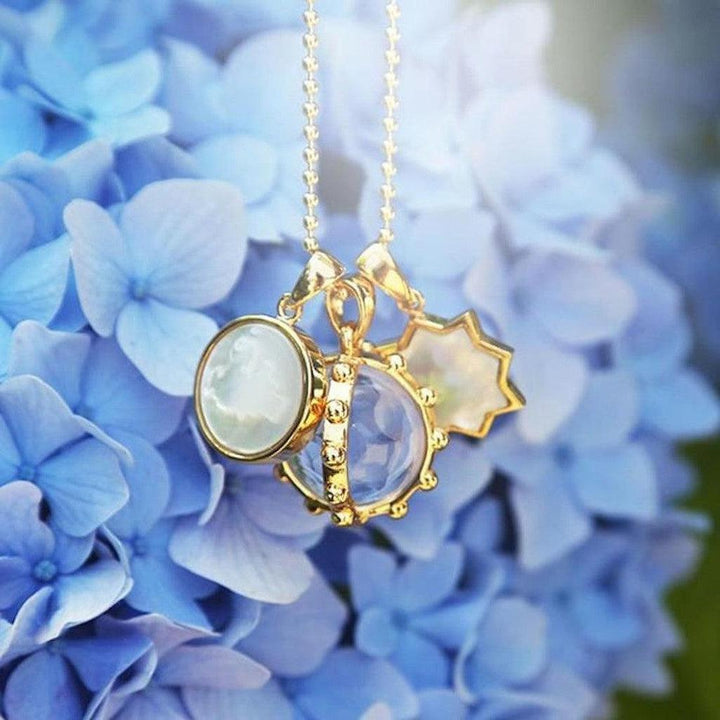 Gold necklace with iridescent charm accents amongst blue hydrangeas.