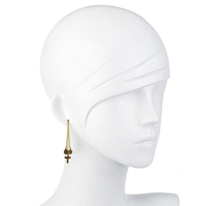 Gold chain earrings adorned with small charms and a cross, shown on a mannequin.