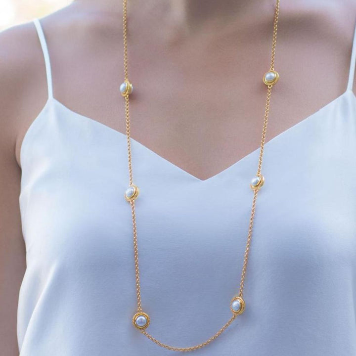 Long gold chain necklace adorned with five pearls, shown on a white top.