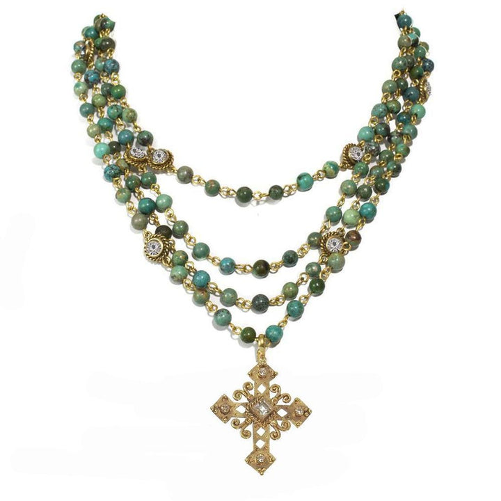 Layered turquoise bead necklace with ornate gold cross pendant.