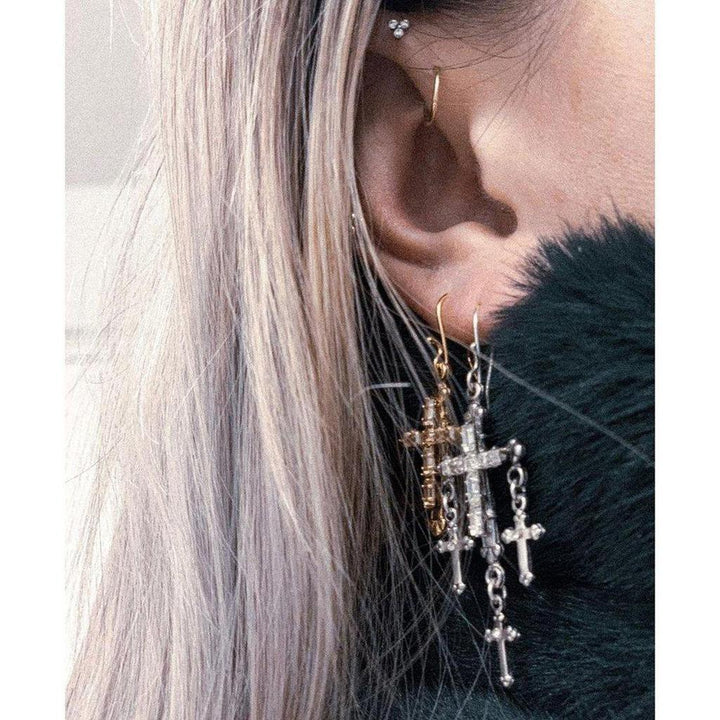 Layered cross earrings; gold and silver, dangling from earlobe against blonde hair.