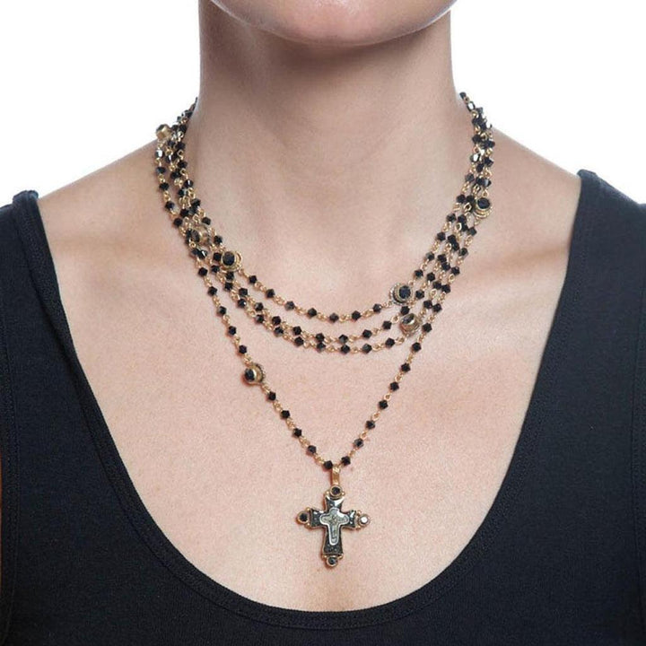 Layered gold necklace featuring black beads and a detailed cross pendant.