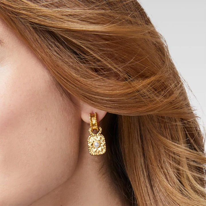 Gold hoop earrings with a square pearl charm, worn against auburn hair.