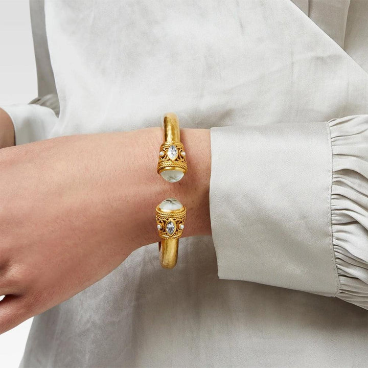 Gold cuff bracelet with semi-precious stones, worn on a wrist.