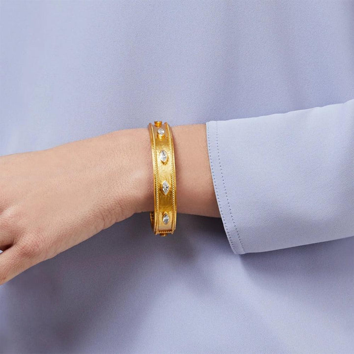 Gold hinged bangle bracelet adorned with clear gemstones, shown on a wrist.